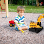 Photo of adorable 3 years old toddler boy playing with sand and you truck and trailer in park. Child digging and building in sandpit