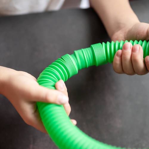anti stress sensory pop tube toys in children’s hands. little happy kids plays with a poptube toy on a black table. toddlers holding and playing pop tubes red and green bright color, trend 2021 year