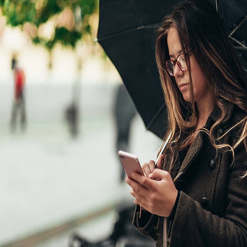 Beautiful young woman using smartphone and holding an umbrella